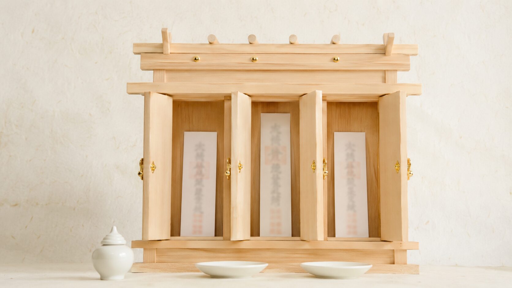 ivory washi 背景に painterly な三社造り神棚の正面、3 つの扉がそれぞれ穏やかに開き、中央に少し背の高い神宮大麻・右に氏神・左に崇敬神社の神札が各扉に1枚ずつ配置された構図、手前左に1個の榊立て、手前右に1個の水玉、神札の並べ方を明示的に示す静物