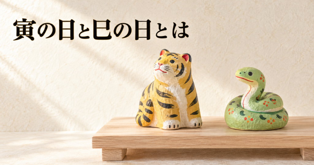 素木の低い台に、郷土玩具の張子の虎と、とぐろを巻いた張子の蛇が少し間をあけて並ぶ静物のイメージ画像。背景は朝の光が差す明るい生成りの和紙の壁で、左上に「寅の日と巳の日とは」の横書きタイトル。毘沙門天と弁才天のお使いとされる虎と蛇で二つの日を象徴するアイキャッチ画像。